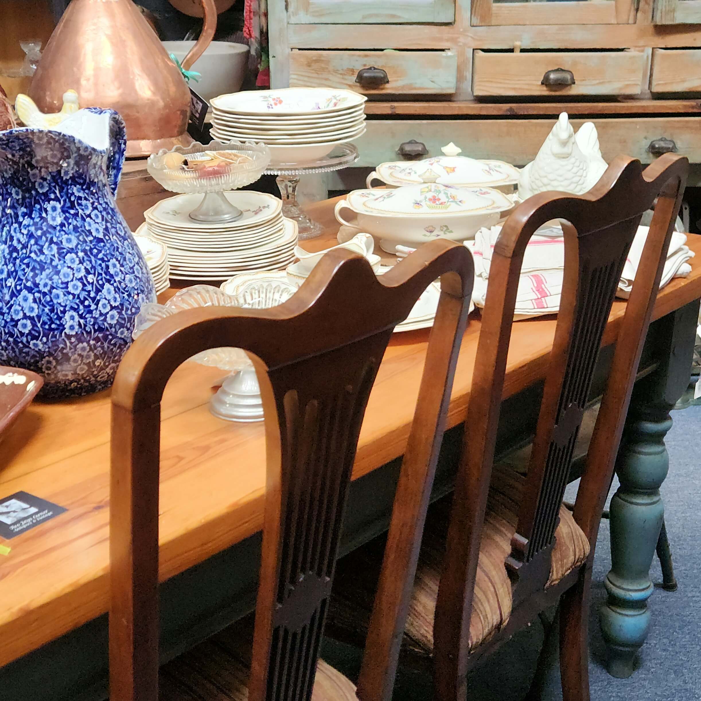 Table
                      and chairs with dinner service on top with a
                      dresser in the background